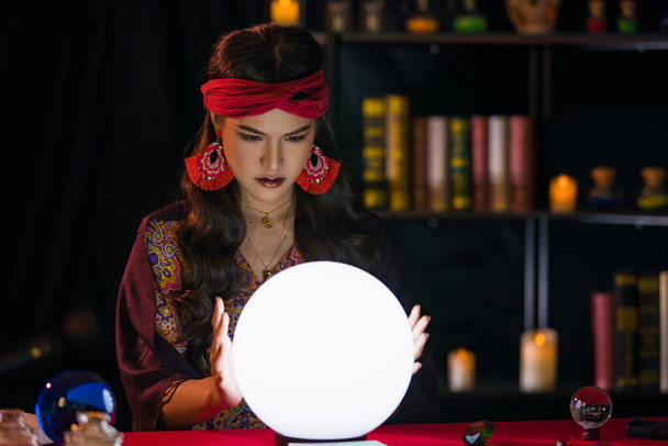 Femme asiatique avec des accessoires occultes lire l'avenir et travailler avec boule de cristal lumineux dans la chambre noire - Photo, image