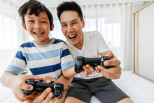 El padre y el hijo en la cama de la familia asiática se divierten y feliz jugando videojuegos en la cama en la habitación. Concepto en unas vacaciones - Foto, imagen