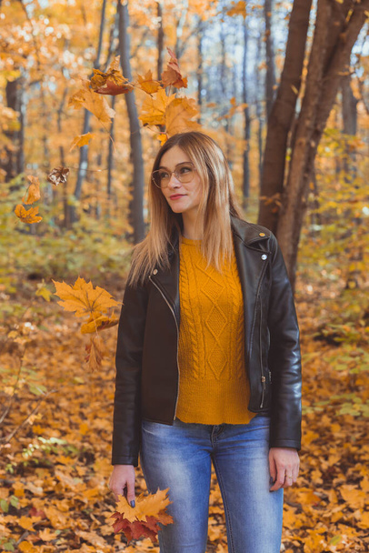 Aranyos mosolygós nő őszi levelekkel az őszi parkban. Szezonális, életmód és szabadidő koncepció. - Fotó, kép