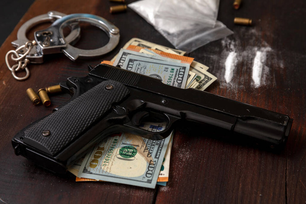 Drugssmokkel en -handel, handboeien, pistoolgeld en cocaïnepakketjes op houten tafelondergrond. Illegale handel in en aanhouding van stoffen - Foto, afbeelding