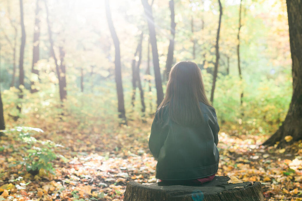Дитяча дівчинка сидить на самоті на дерев'яному пні під час прогулянки по лісу в осінній день. Самотність і меланхолія концепція
. - Фото, зображення