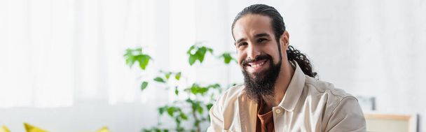 бородатий іспаномовний чоловік посміхається на камеру вдома, банер
 - Фото, зображення