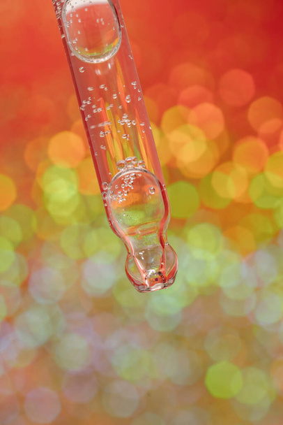 Pipette with serum on a red holiday background with bokeh. - Photo, image