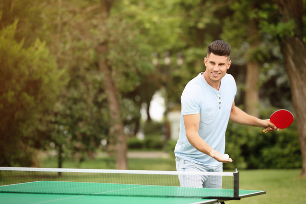 Happy man playing ping pong outdoors on summer day - Фото, изображение