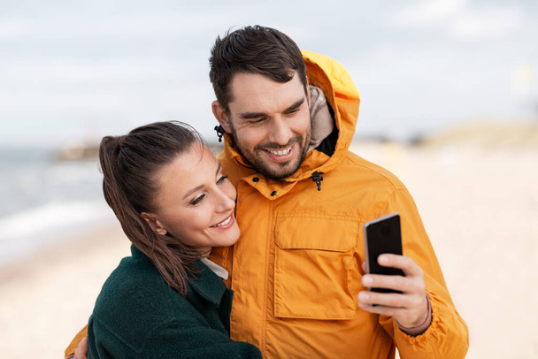 couple with smartphone on autumn beach - Zdjęcie, obraz