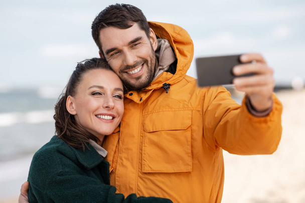 couple with smartphone on autumn beach - Foto, afbeelding
