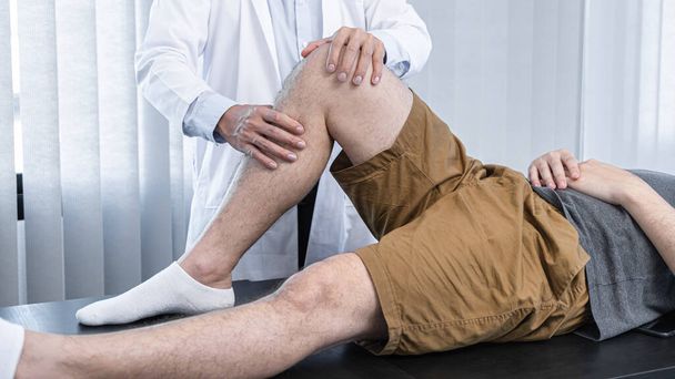 Jovem asiático fisioterapeuta verificando articulação do joelho com lesão para dar tratamento e terapias de reabilitação na clínica - Foto, Imagem
