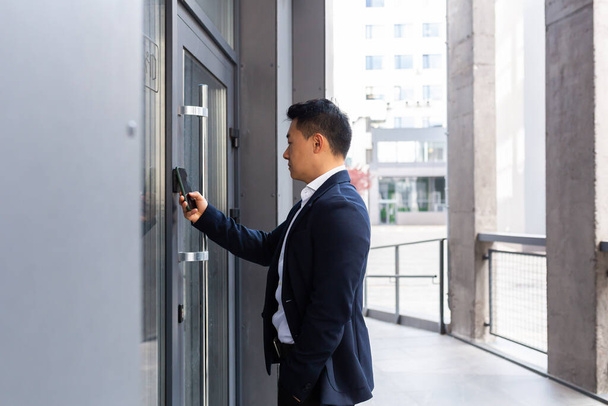Un homme d'affaires asiatique prospère ouvre la porte du centre de bureau en utilisant un smartphone et une application NFC - Photo, image