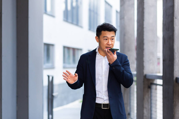 angry and serious Successful Asian businessman explains information to employees using phone, speaks near office outside - Photo, image