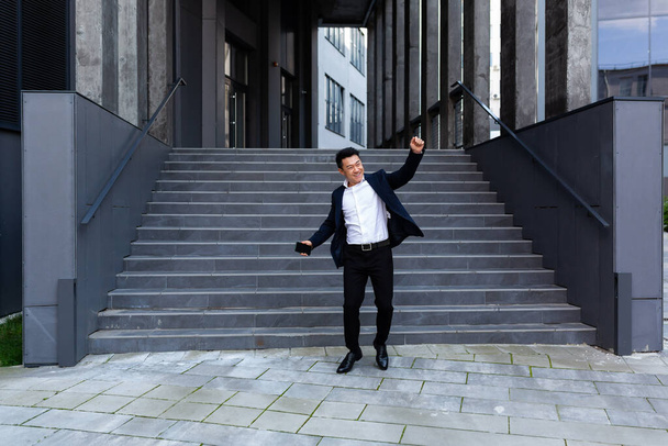 Szczęśliwy i wesoły biznesmen azjatycki taniec w pobliżu biura cieszy się zwycięstwem i sukcesem - Zdjęcie, obraz