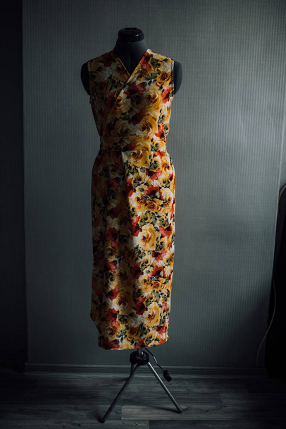 geel-rode jurk gemaakt van natuurlijke stof op een etalagepop. foto van kleding in het atelier. gladde naden en steken zijn gestikt met draad. de naaister maakt individuele kleermakerij thuis. - Foto, afbeelding