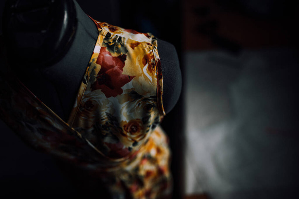 bovenaanzicht van een geel-rode jurk gemaakt van natuurlijke stof op een etalagepop. close-up foto van kleding. gladde naden en steken zijn gestikt met draad. de naaister maakt individuele kleermakerij thuis. - Foto, afbeelding