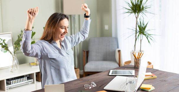 Young woman holding hands up yelling looking at screen of laptop celebrating achievement successfully completed job project presentation - Photo, Image