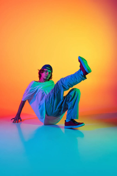 Close-up portrait of young man, hip-hop dancer in stylish clothes in action isolated on colorful background at dance hall in neon light. - Foto, Imagen