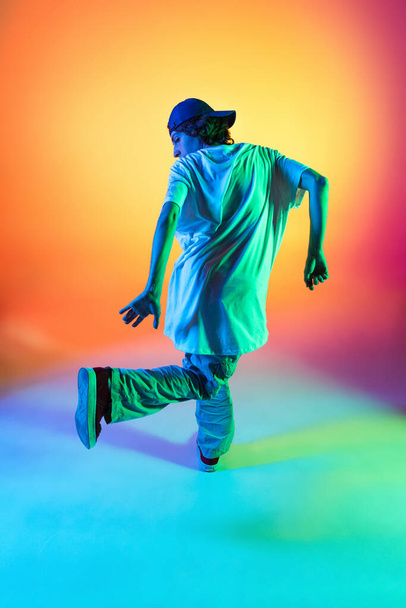 Close-up portrait of young man, hip-hop dancer in stylish clothes in action isolated on colorful background at dance hall in neon light. - Photo, Image