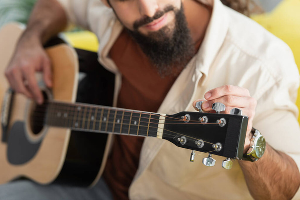 cropped view of blurred musician tunning guitar at home - Foto, imagen