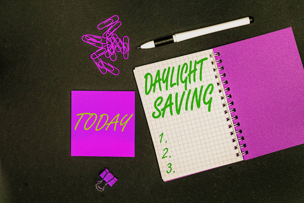 Hand writing sign Daylight Saving. Concept meaning turning the clock ahead as warmer weather approaches Multiple assorted collection office stationery photo placed over table - Photo, Image