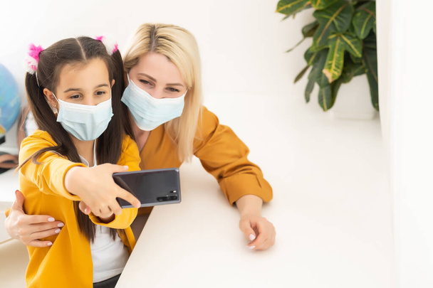 Little girl and her young mother taking a selfie wearing surgical mask. - Photo, Image