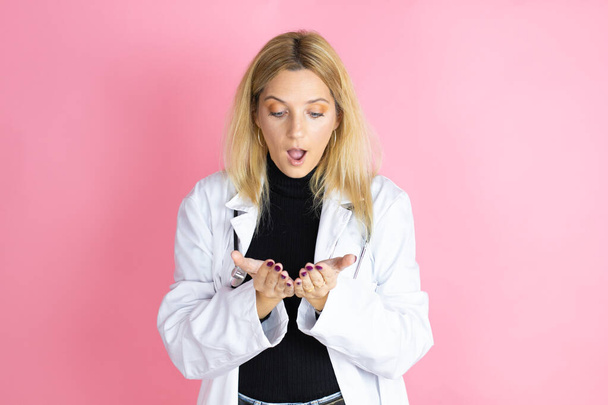 Młoda blondynka doktor kobieta nosząca stetoskop stojąca nad odizolowanym różowym tle Uśmiechnięta dłońmi dłońmi razem otrzymująca lub dająca gest. Przechowywanie i ochrona - Zdjęcie, obraz