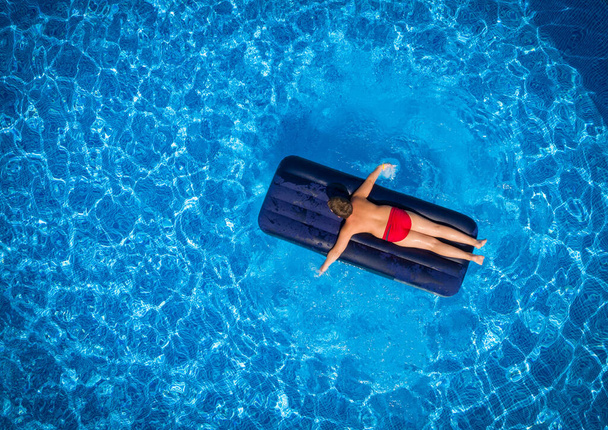 sunbathes boy lying on inflatable mattress in the swimming pool, directly above aerial view - Foto, Bild