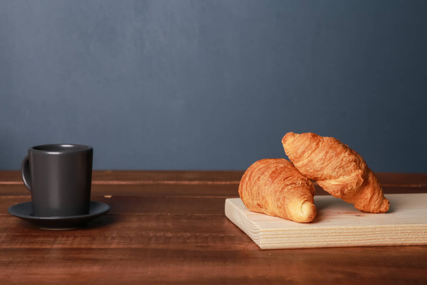 Friss sült croissant, fekete kávé barna fa asztalon, kék fal háttér. Egy csésze eszpresszó, péksütemények a vágódeszkán, közelről. Francia reggeli, reggeli menü, kávézó koncepció - Fotó, kép
