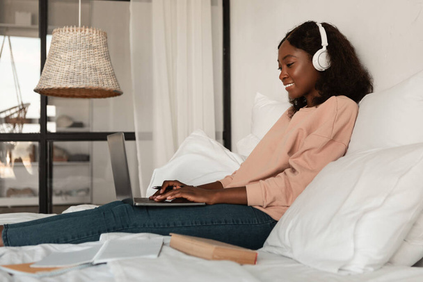 Side-View Of Black Woman Using Laptop Learning Online In Bedroom - Фото, изображение