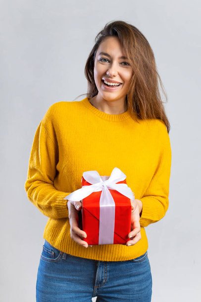 Joyeux jeune femme donnant une boîte-cadeau rouge isolé sur fond gris - Photo, image
