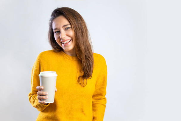 Smiling young woman drinking coffee from a paper cup on white background - Fotoğraf, Görsel