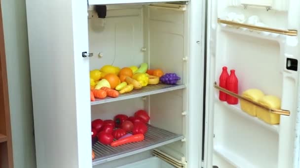 Женская рука открывает игрушечный холодильник, который содержит игрушечные пластиковые овощи и фрукты. Концепция детской образовательной игры. Высококачественные FullHD кадры - Кадры, видео