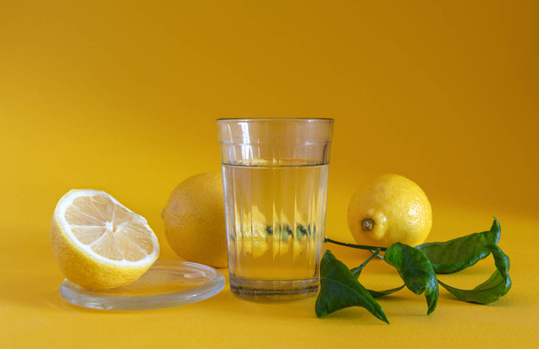 Ένα ποτήρι λεμονάδα και ώριμα λεμόνια σε κίτρινο φόντο. - Φωτογραφία, εικόνα