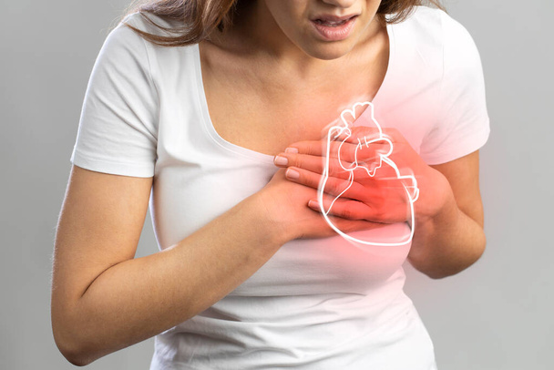 Young woman pressing on chest with painful expression. Severe heartache, having heart attack or painful cramps, heart disease. - Photo, image