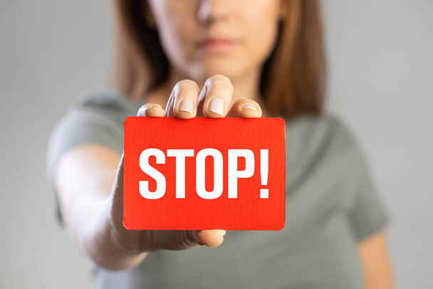 Young woman holding red stop card on gray backgroun - Fotó, kép