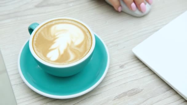 Pausa caffè. Tazza di cappuccino sul tavolo da lavoro con una donna che digita su un computer portatile. Filmati 4k di alta qualità - Filmati, video