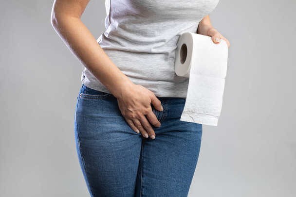 Woman hand holding her crotch lower abdomen and toilet paper roll. Disorder, diarrhea, incontinence - Fotoğraf, Görsel