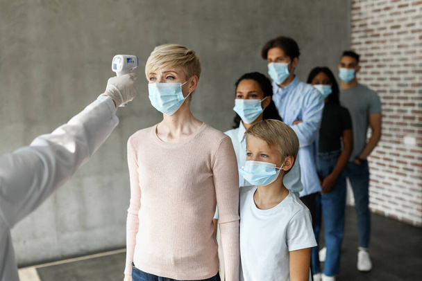 Багаторасова група пацієнтів у масках для обличчя, що перевіряють температуру тіла
 - Фото, зображення