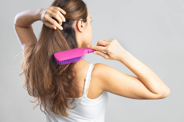Back view of brunette beautiful woman brushing long straight healthy and shiny hair with comb - Foto, Bild