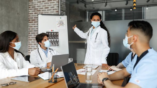 Πολυφυλετική ομάδα γιατρών με μάσκες προσώπου που πραγματοποιούν ιατρικό συνέδριο - Φωτογραφία, εικόνα