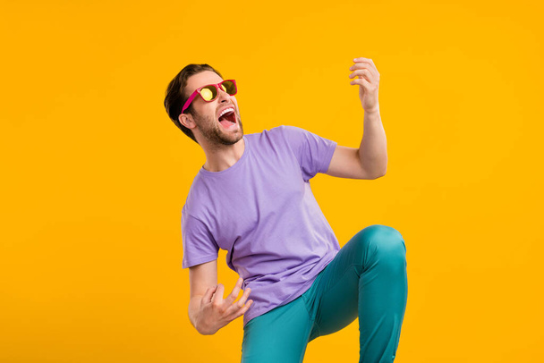 Photo of careless rocker guy play imaginary guitar scream wear sunglass purple t-shirt isolated yellow color background - 写真・画像