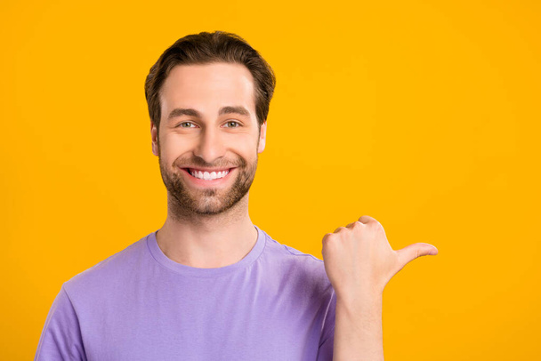 Photo of handsome guy indicate forefinger empty space wear violet t-shirt isolated yellow color background - Foto, afbeelding