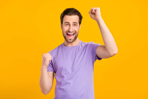 Photo of cheerful astonished guy celebrate victory open mouth wear purple t-shirt isolated yellow color background - 写真・画像