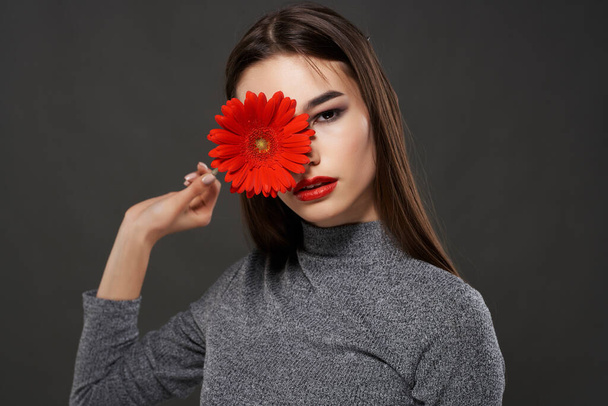 jolie brune fleur rouge près du visage maquillage fond sombre - Photo, image
