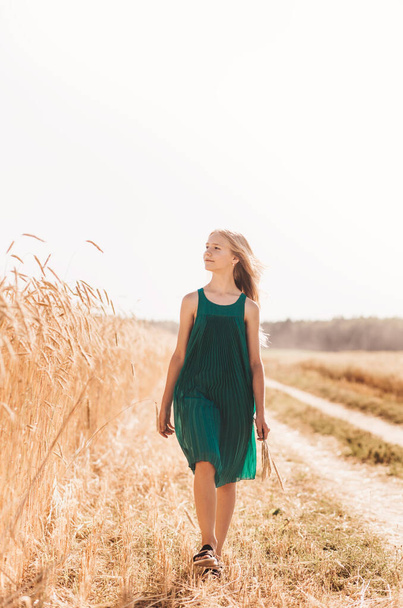 Beautiful teenage girl with long white hair walking through a wheat field on a sunny day - Фото, изображение