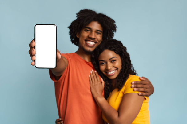 Любящая чёрная пара обнимается и показывает смартфон, макет - Фото, изображение