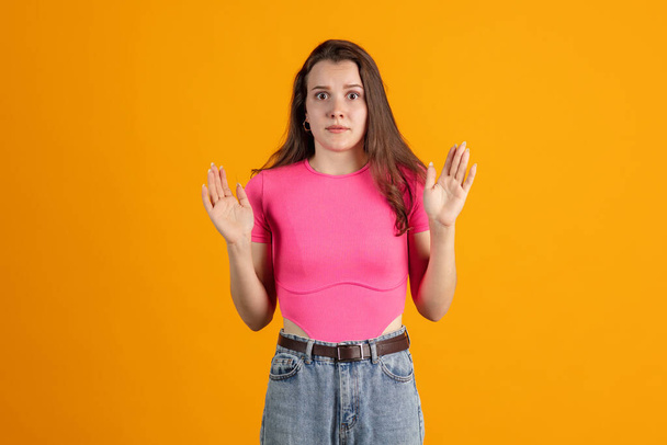 Cropped portrait of young beautiful girl wearing pink shirt isolated over orange studio background - Foto, afbeelding
