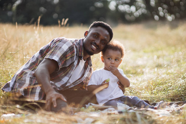 Cute african boy eating grape during summer picnic with dad - Fotografie, Obrázek