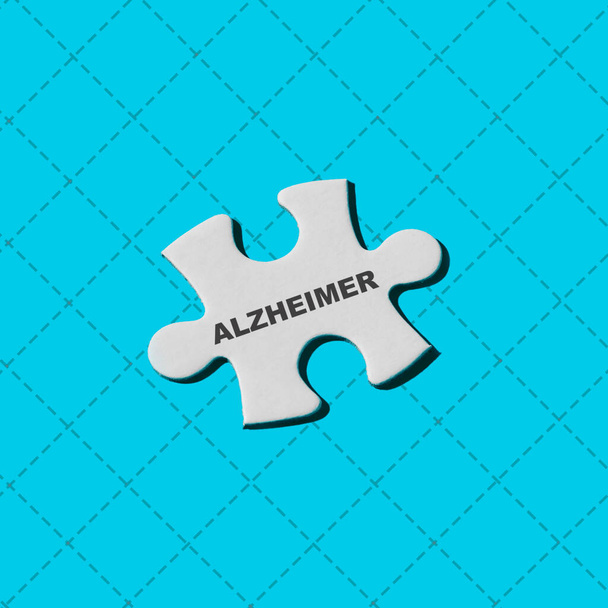 ένα λευκό κομμάτι παζλ με τη λέξη alzheimer γραμμένο σε ένα μπλε φόντο - Φωτογραφία, εικόνα
