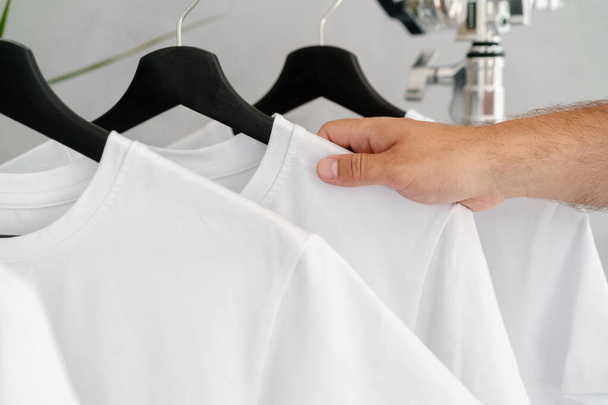 Male hand holds hanger with blank white t-shirt - Foto, imagen