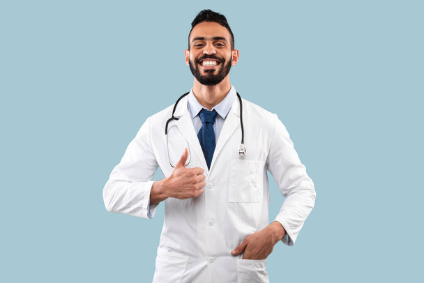 Άραβας γιατρός αρσενικό gesturing αντίχειρες πάνω από μπλε φόντο - Φωτογραφία, εικόνα
