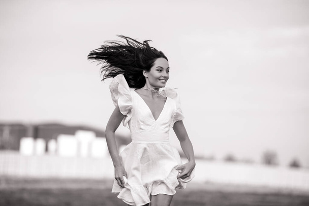 Young joyful woman in white dress runs in meadow on summer sunny day. Black and white image. Closeup. - Foto, Bild