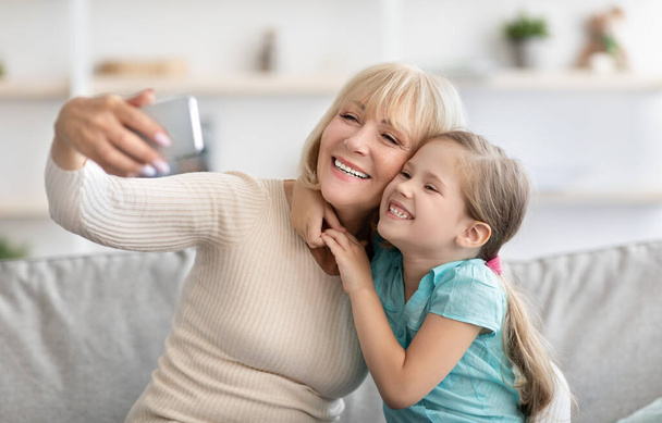 Selfie familiar. Retrato de la familia de varias generaciones tomando fotos de selfies juntos en casa en el interior. Feliz abuela posando con su nieto usando el teléfono móvil. Vinculación y concepto de estilo de vida - Foto, imagen